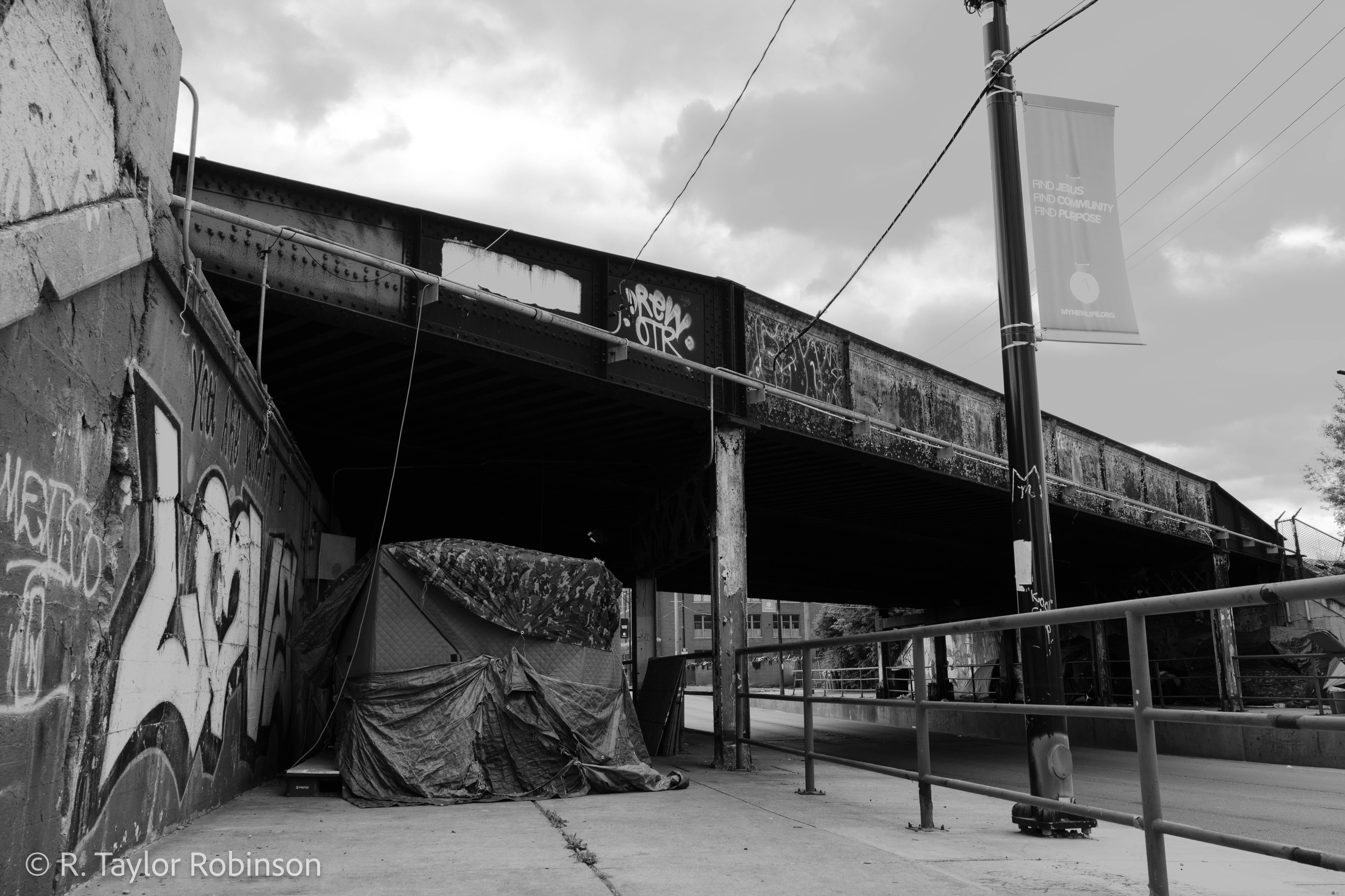 May 19, on W Division St., just a block from the New Life Covenant Church, sits the bright red tent of Israel Gonzalez, 34, just under the train tracks, where he has lived for a year and a half after serving 121 months in a federal penitentiary. A mural on the wall above reads "YOU ARE WORTHY OF LOVE."