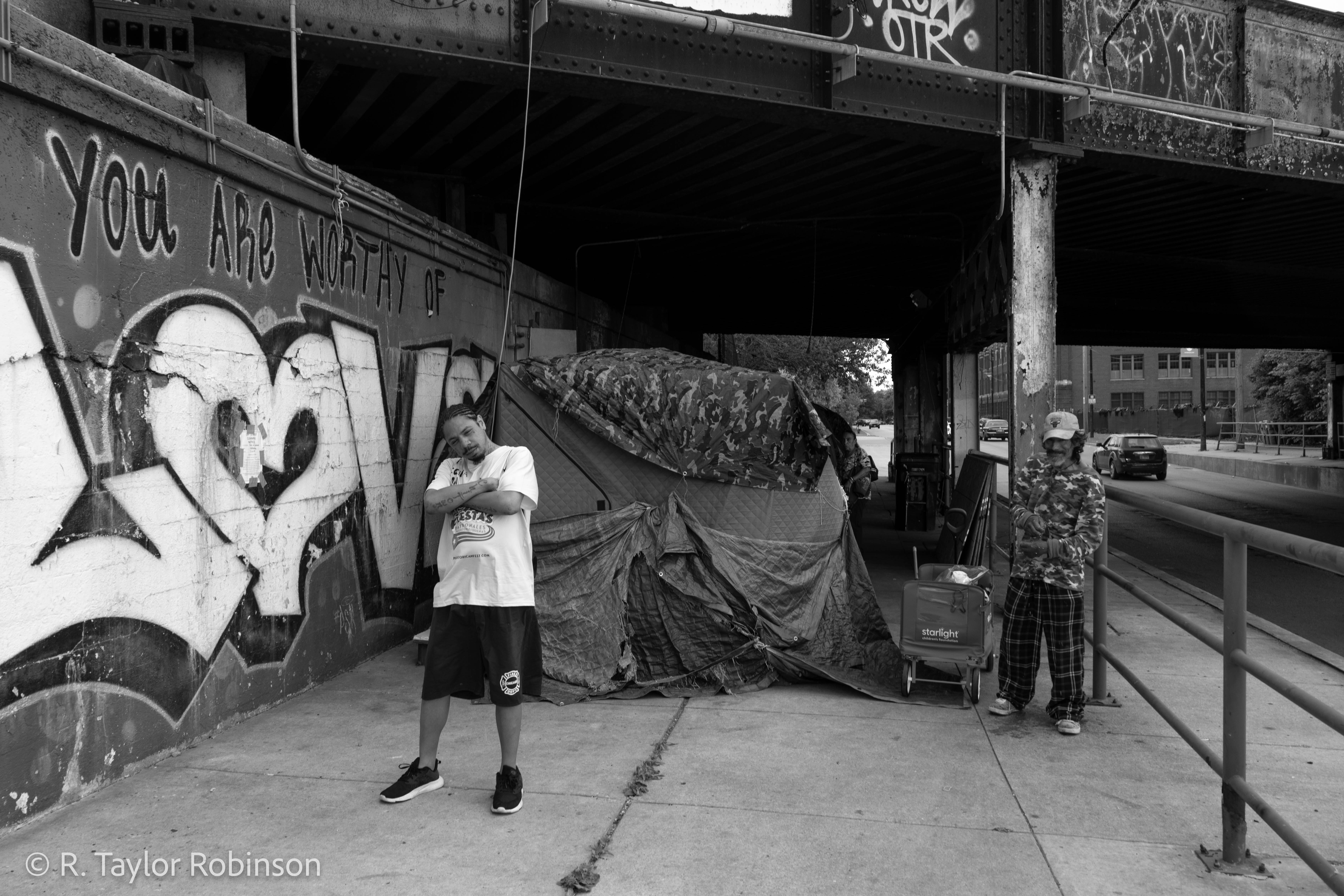 Gonzalez (left) poses on a hot and humid Tuesday outside of his tent next to Paco (right), who said his real name is Lenin "like the communist." Gonzalez said the tent is retractable so it stays "kinda warm" in the winter, but he needs to get a heater. To get by, he does Doordash and Uber Eats on his bicycle, but the bike was stolen three days before.