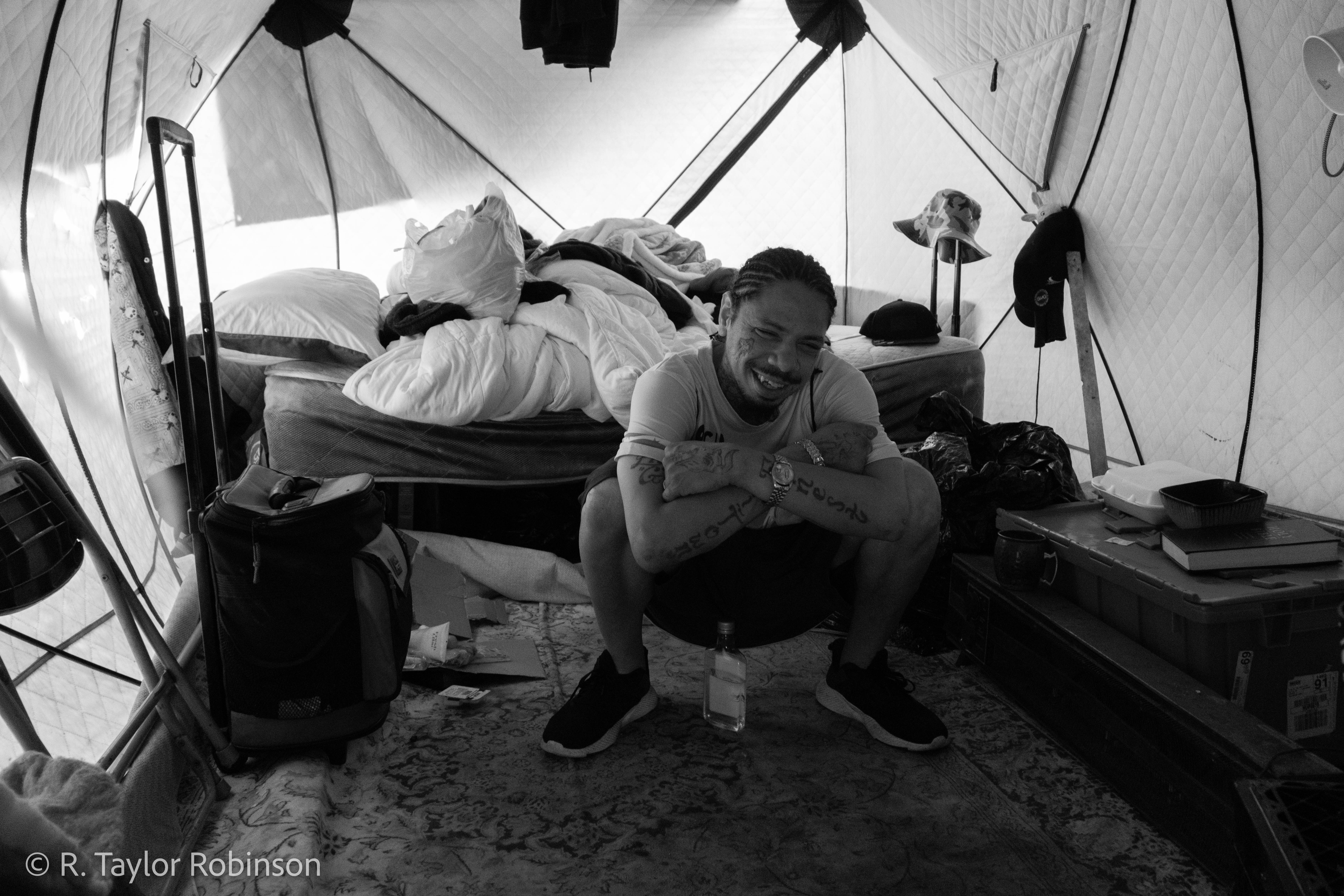 Gonzalez poses inside of his tent, which has a rug stretched out on the floor under his bed, a few miscellaneous containers, a microwave and a fridge. In 2021, when he was still in prison, he said he had a young roommate about 18 years old with multiple life sentences, the kid would rock in bed every night. He was scared at first, not knowing why the kid was rocking, until, according to Gonzalez, one day the kid turned to him and said, "would you pray with me? I didn't do that crime. I was with somebody that did it."