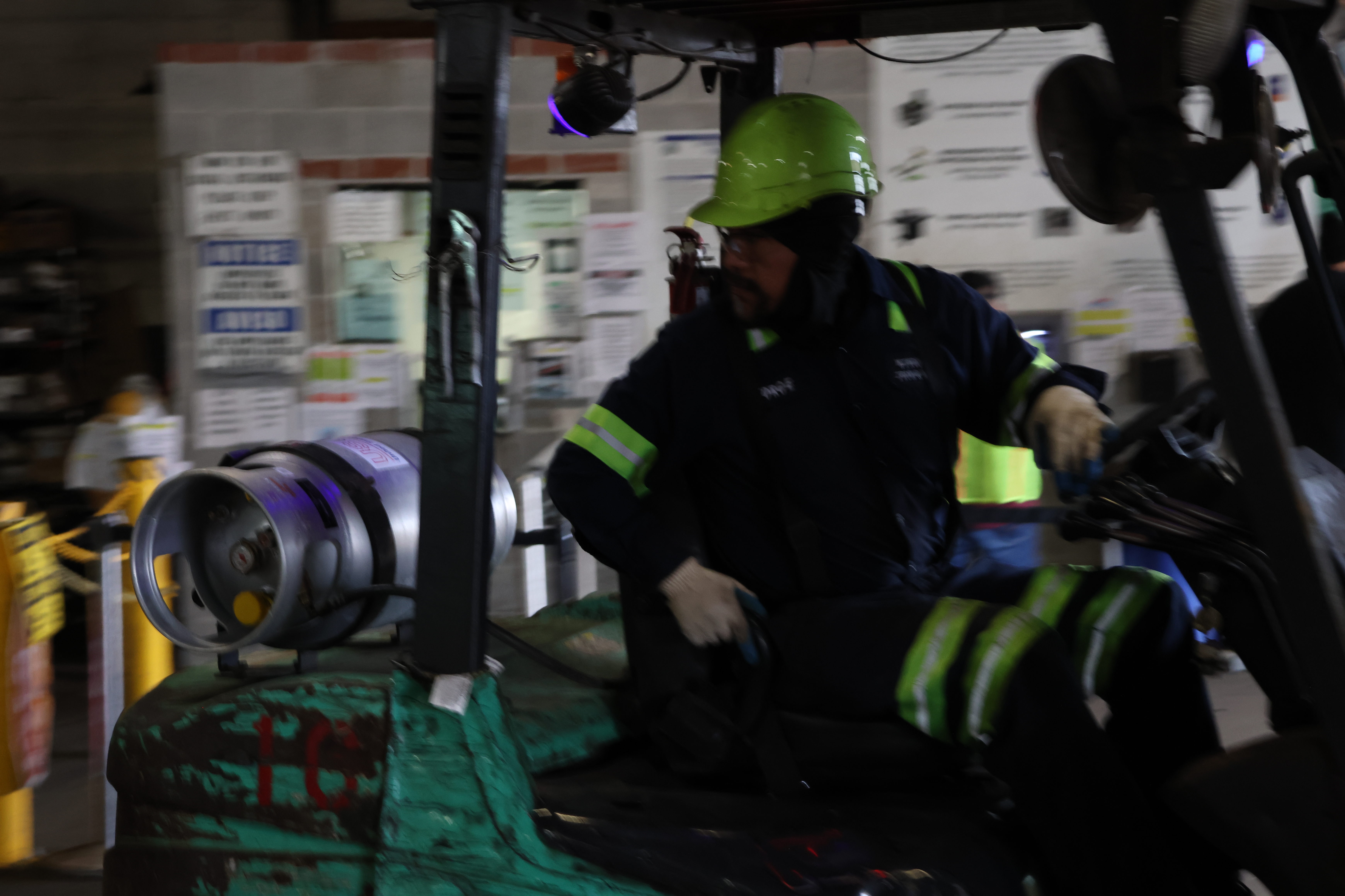 The forklift operator checks his trailer as he zooms past on his forklift. He is done ferrying the canisters.